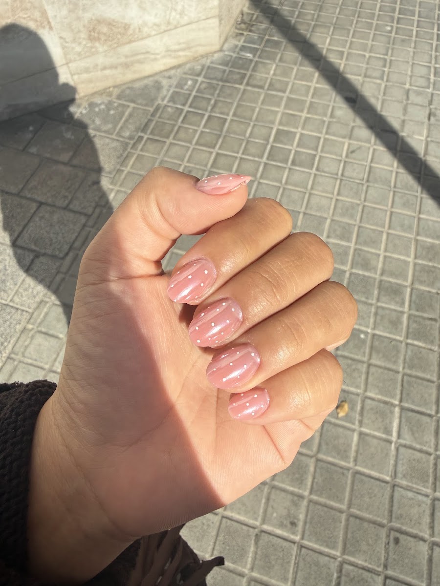Mano cerrada mostrando uñas rosadas con puntos blancos sobre pavimento gris