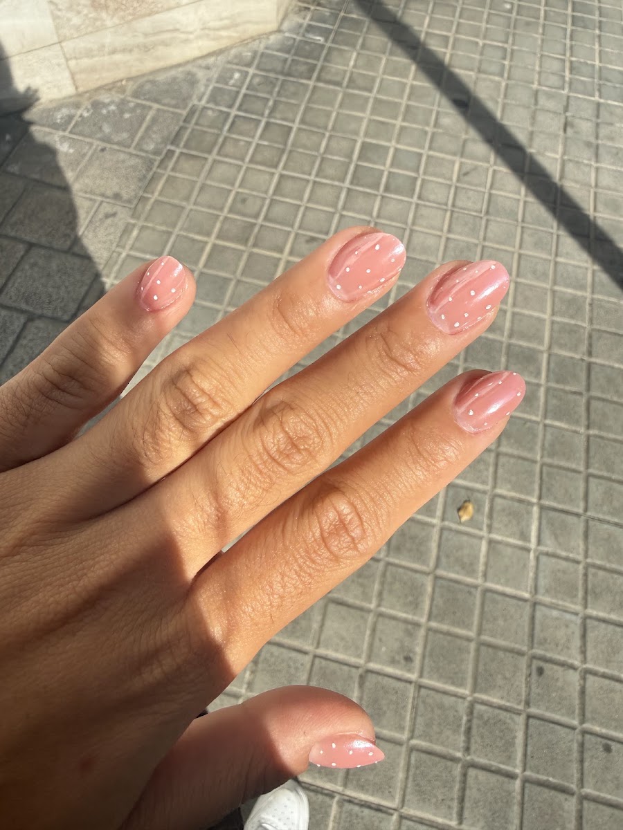 Mano extendida con uñas cortas rosadas decoradas con puntos blancos sobre baldosas