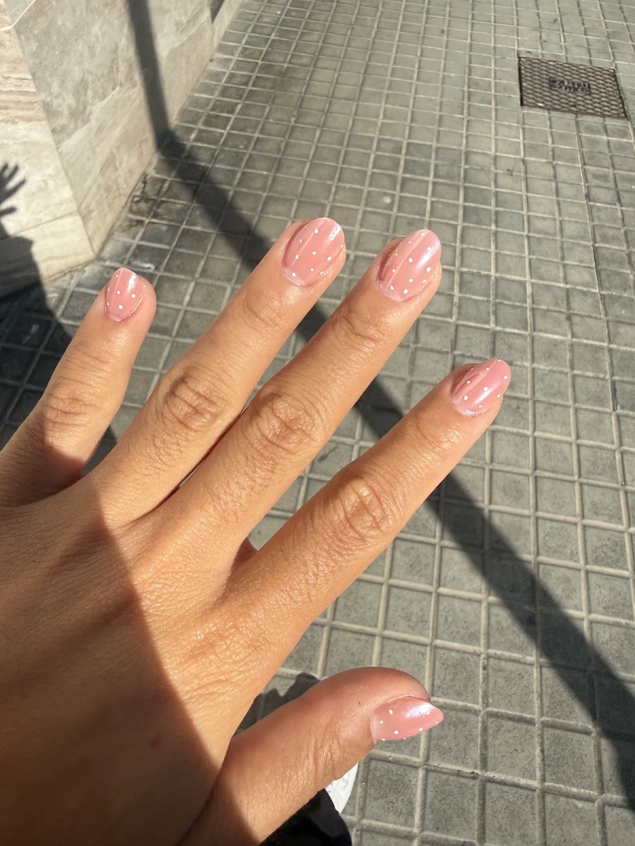 Mano con uñas cortas rosadas con puntos blancos decorativos sobre pavimento