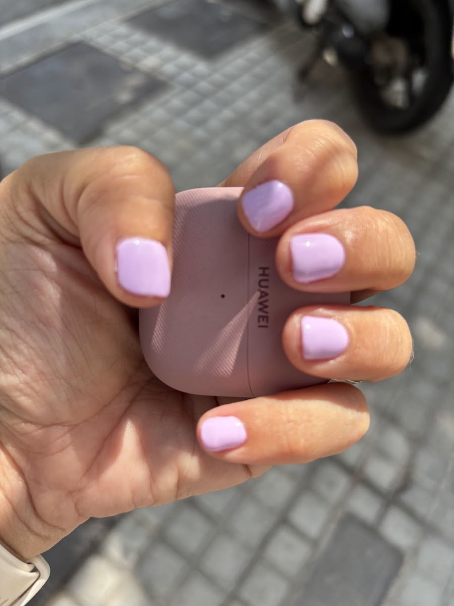 Mano sosteniendo un móvil rosa, con uñas cortas moradas, sobre pavimento