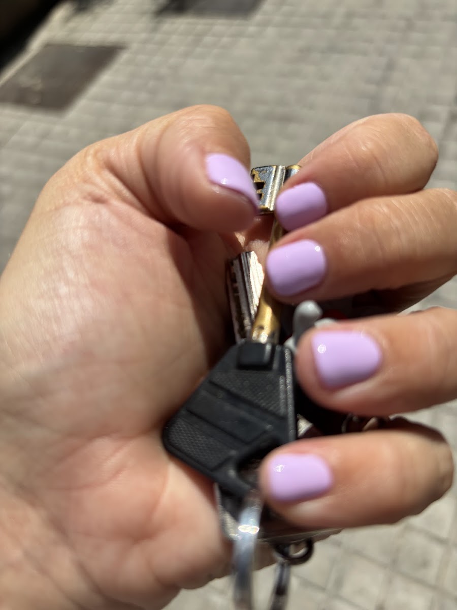 Mano sosteniendo unas llaves, con uñas cortas en color lila mate