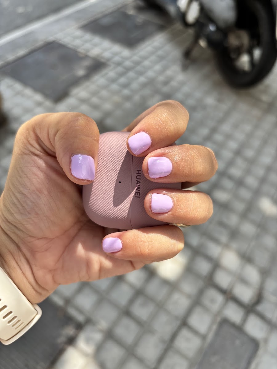 Mano con uñas lila sosteniendo un móvil rosa sobre pavimento